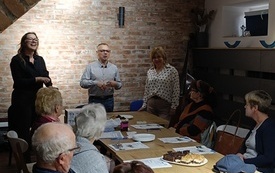 Seniorzy siedzący przy stołach w sali. burmistrz stojący i przemawiający