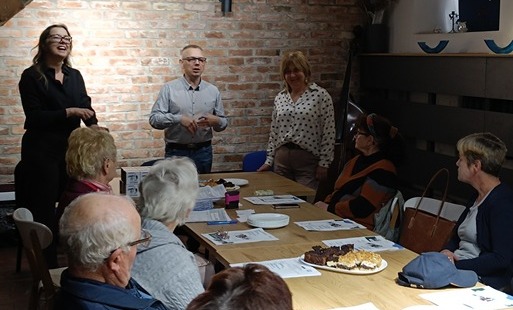 Seniorzy siedzący przy stołach w sali. burmistrz stojący i przemawiający